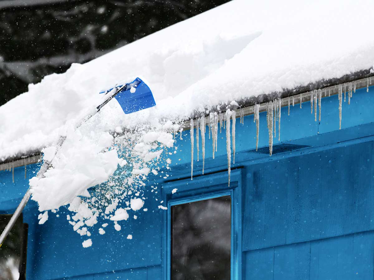 Accumulation de neige et de glace sur le toit et la gouttière d’une maison verte.
